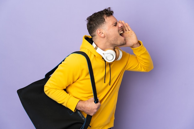 Uomo caucasico di giovane sport con la borsa isolata viola che grida con la bocca spalancata a lato
