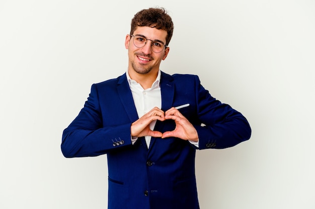 Uomo caucasico di giovani affari isolato sul muro bianco sorridente e mostrando una forma di cuore con le mani.