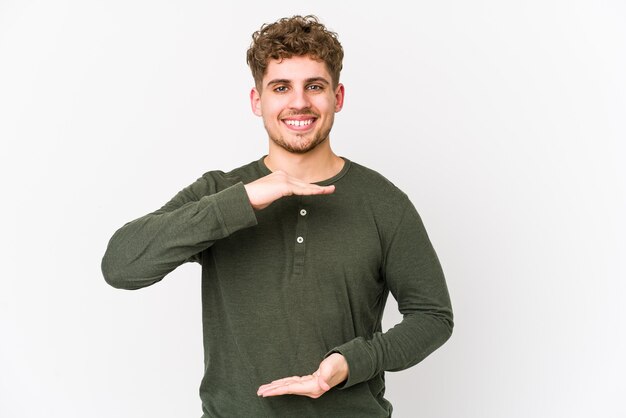 Uomo caucasico di giovani capelli ricci biondi isolato tenendo qualcosa con entrambe le mani, presentazione del prodotto.