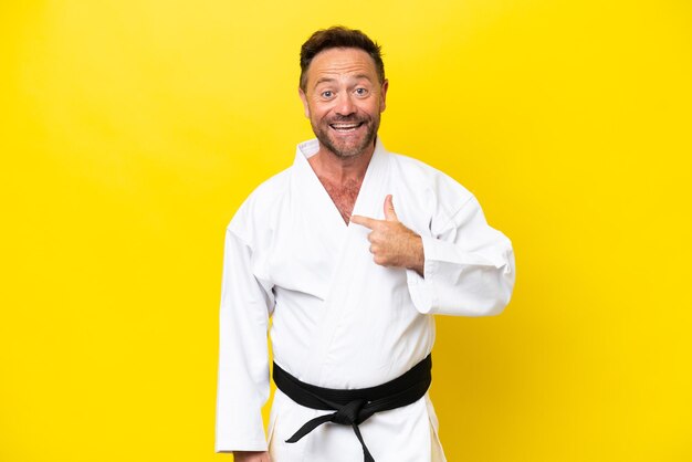 Uomo caucasico di mezza età che fa karate isolato su sfondo giallo con espressione facciale a sorpresa