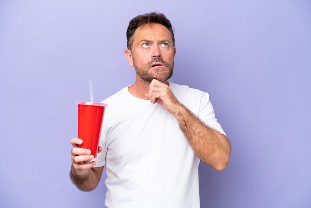 Uomo caucasico di mezza età che tiene la soda isolata su sfondo viola e alza lo sguardo