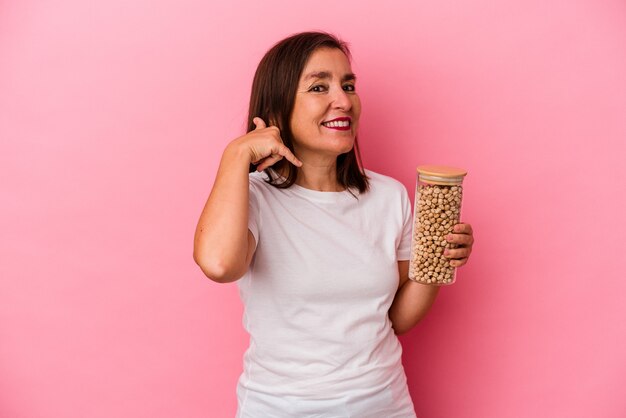 Uomo caucasico di mezza età che tiene un barattolo di ceci isolato su sfondo rosa che mostra un gesto di telefonata con le dita.