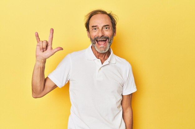 Uomo caucasico di mezza età in studio giallo che mostra un gesto di corna come concetto di rivoluzione