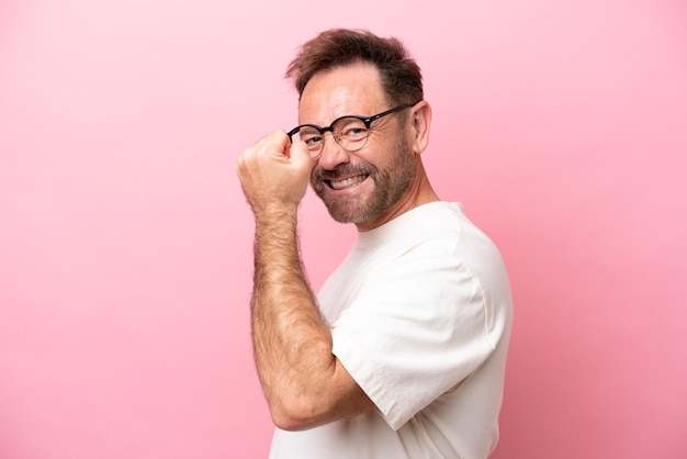 Uomo caucasico di mezza età isolato su sfondo rosa Con gli occhiali e celebrando una vittoria