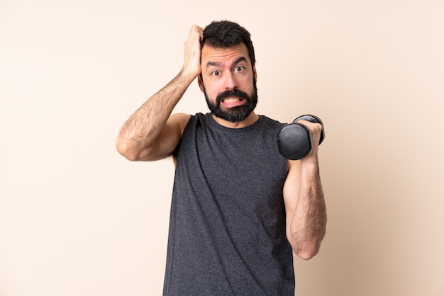 Uomo caucasico di sport con la barba che fa sollevamento pesi sopra la parete isolata che fa gesto nervoso