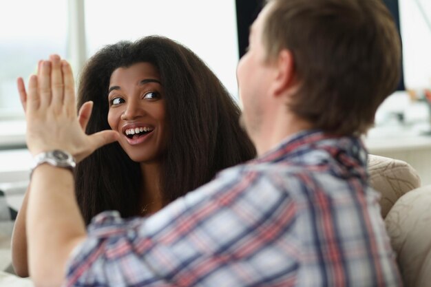 Uomo caucasico e donna afroamericana seduta sul divano e dando il cinque