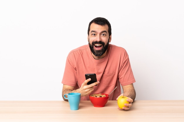 Uomo caucasico facendo colazione in un tavolo sorpreso e inviando un messaggio.