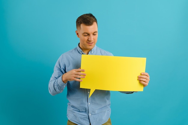 Uomo caucasico gioioso che mostra un cartello bianco su sfondo blu per studio mockup per il design