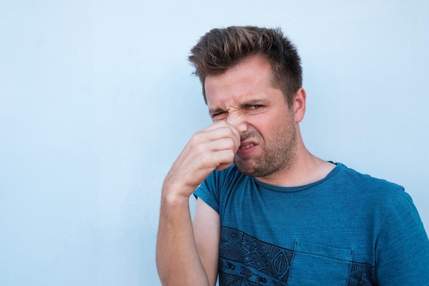 Uomo caucasico in camicia blu che chiude il naso a causa del cattivo odore