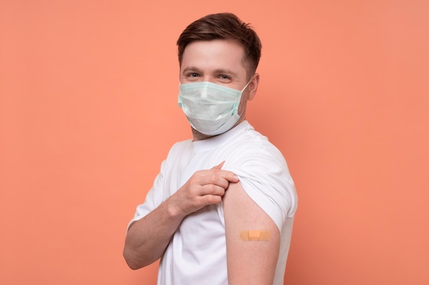 Uomo caucasico in maschera medica che mostra il suo braccio vaccinato Ha ricevuto un vaccino corona guardando la fotocamera Studio girato