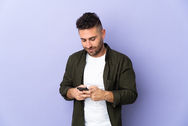 Uomo caucasico isolato sulla parete viola inviando un messaggio con il cellulare