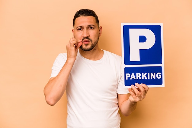 Uomo caucasico ispanico con cartello di parcheggio isolato su sfondo beige con le dita sulle labbra mantenendo un segreto