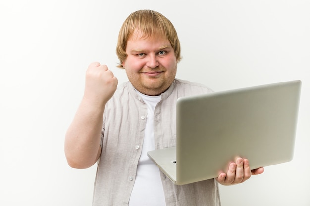 Uomo caucasico plus size in possesso di un computer portatile che mostra il pugno, aggressivo espressione facciale.