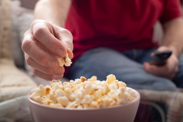 Uomo caucasico seduto sul divano con popcorn e telecomando della tv