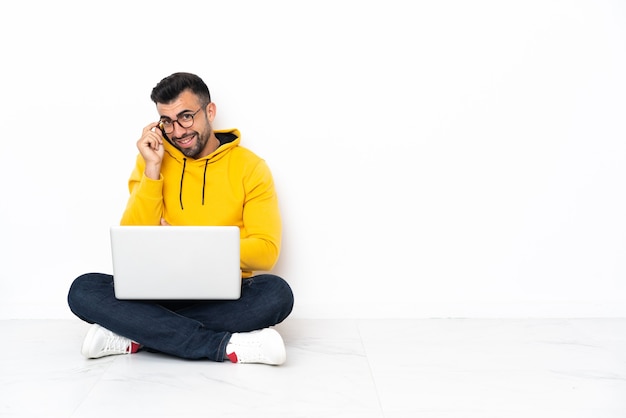 Uomo caucasico seduto sul pavimento con il suo laptop con gli occhiali e felice