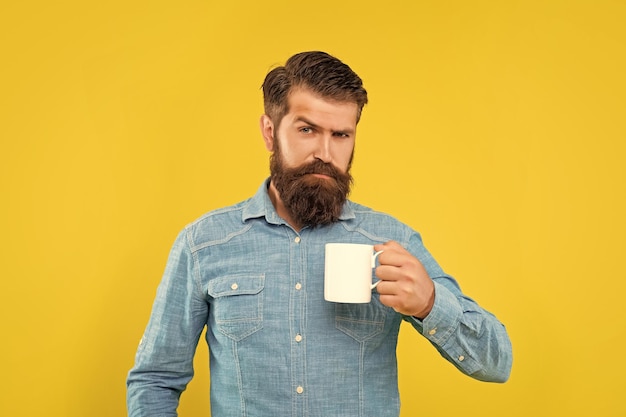 Uomo caucasico serio che tiene la pausa tè del fondo giallo della tazza