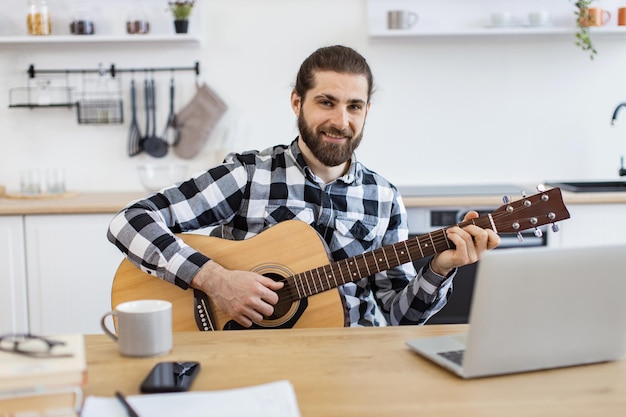 Uomo caucasico sorridente che impara a suonare uno strumento usando lezioni online sul portatile