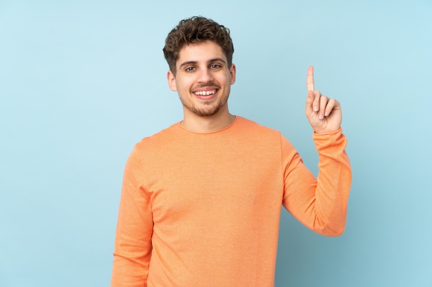 Uomo caucasico su blu mostrando e sollevando un dito in segno del meglio