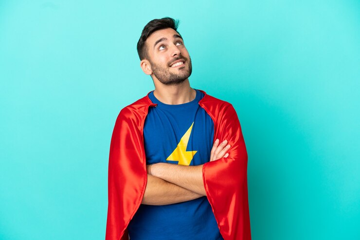 Foto uomo caucasico super eroe isolato su sfondo blu che guarda in alto mentre sorride