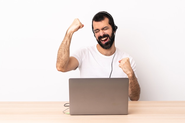 Uomo caucasico telemarketer che lavora con un auricolare e con il computer portatile che celebra una vittoria.