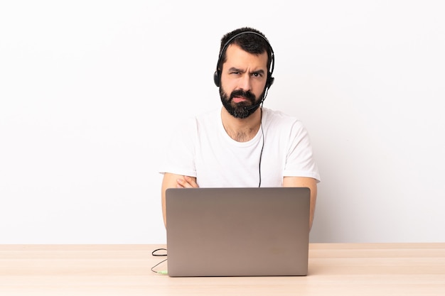 Uomo caucasico telemarketer che lavora con un auricolare e con il computer portatile con espressione infelice.