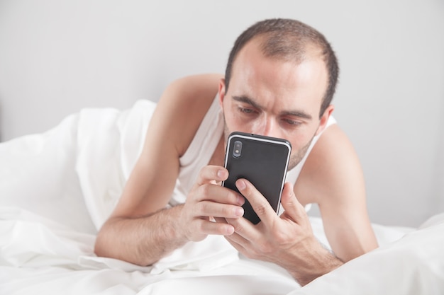 Uomo caucasico utilizzando smartphone a letto.