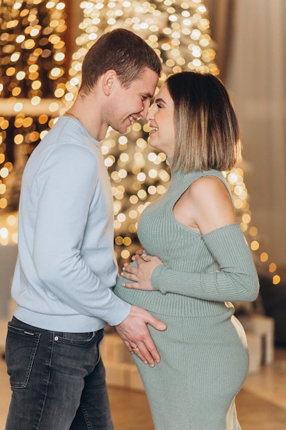 uomo che abbraccia donna incinta vicino all'albero di Natale