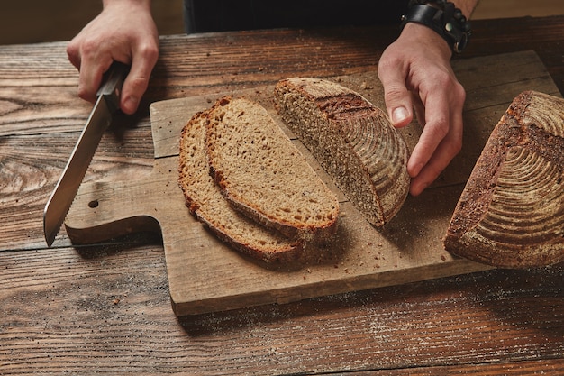 Uomo che affetta il pane di grano di segale fresco gustoso concetto di mangiare sano