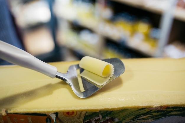 Uomo che affetta un piccolo pezzo di formaggio per il gusto Un giovane lavoratore usa un coltello speciale per il formaggio