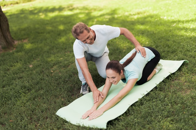 Uomo che aiuta la ragazza. Warm up donna sul tappeto per lo yoga.