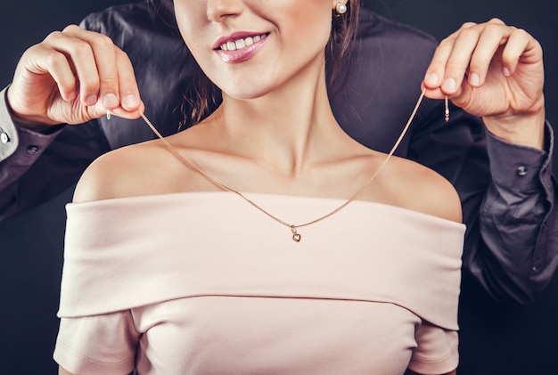 Uomo che aiuta la sua ragazza a provare una collana d'oro. Regalo per San Valentino.