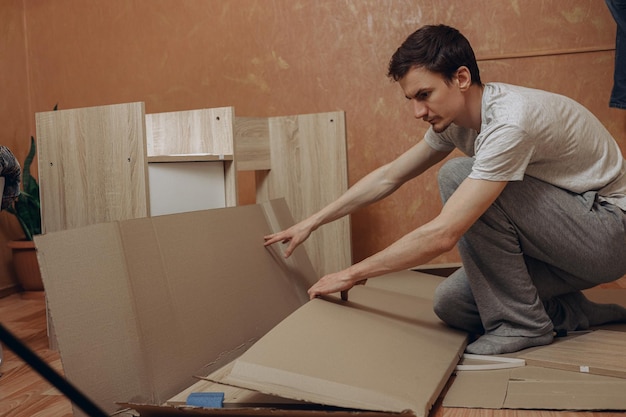 Uomo che apre una scatola di cartone con nuovi mobili per il processo di assemblaggio in piano