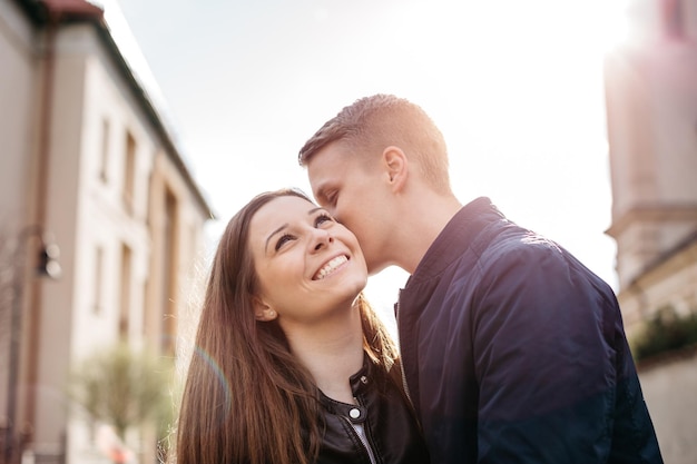 Uomo che bacia una donna sulla guancia mentre si trova in mezzo agli edifici contro il cielo