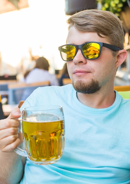 Uomo che beve birra. Bel giovane che beve birra mentre è seduto al caffè all'aperto