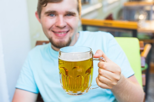 Uomo che beve birra. Bel giovane hipster che beve birra mentre è seduto al bar all'aperto