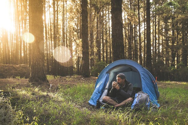 Uomo che beve caffè mentre è seduto in tenda nella foresta