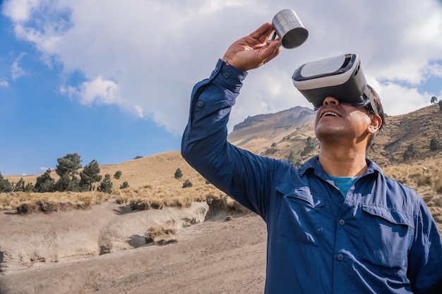 Uomo che beve una tazza di caffè con gli occhiali VR sulla montagna