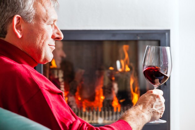 Uomo che beve vino rosso sul camino