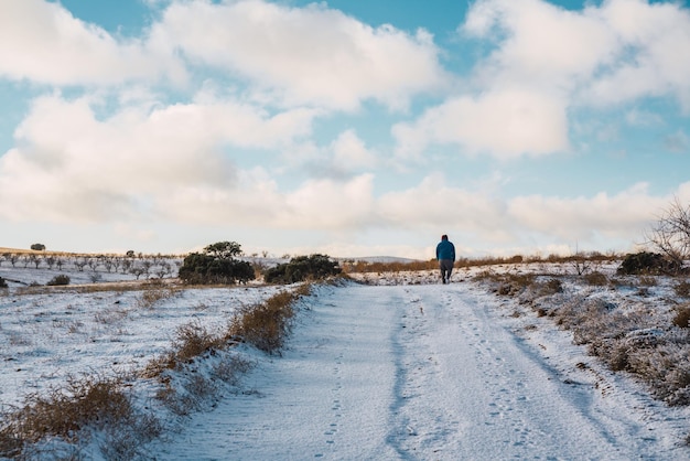 Uomo che cammina in mezzo al campo su una strada innevata