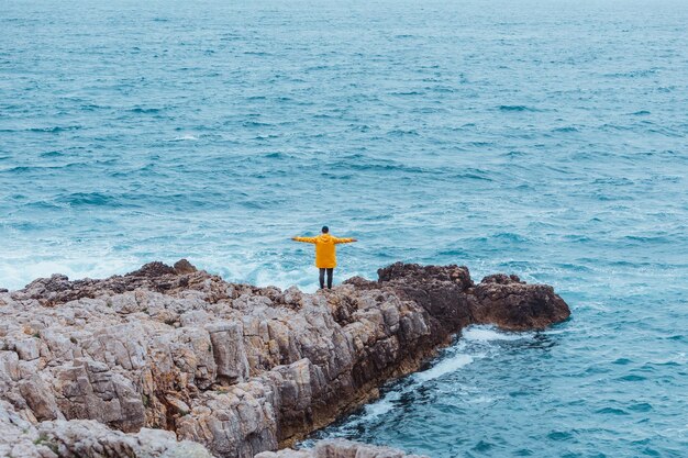 Uomo che cammina sulla roccia verso il mare in tempesta