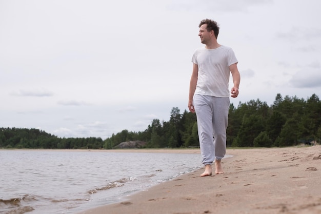 Uomo che cammina sulla spiaggia sabbiosa che guarda sull'acqua