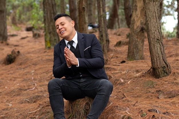 Uomo che canta con gli occhi chiusi e intrecciando le mani. Seduto in una bellissima foresta.