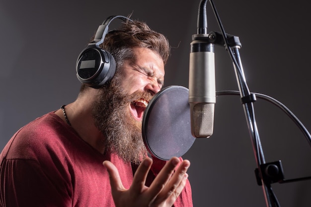 Uomo che canta in uno studio di registrazione uomo barbuto espressivo con il segno del karaoke del produttore del suono del microfono...