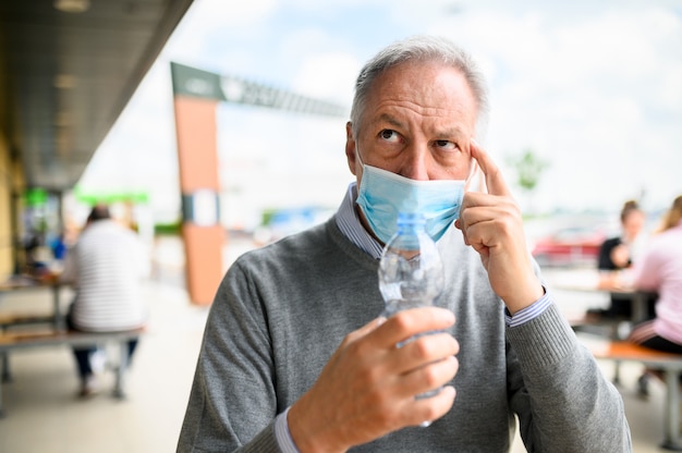 Uomo che cerca di bere una bottiglia di acqua che indossa una maschera