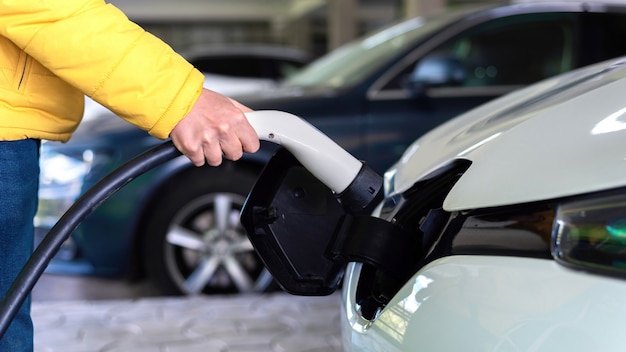 Uomo che collega il caricatore a un'auto elettrica bianca