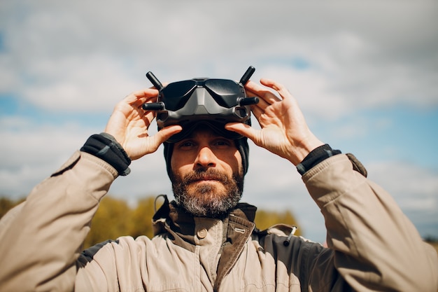 Uomo che controlla il drone quadricottero fpv per la fotografia aerea e la videografia con il telecomando dell'antenna degli occhiali.