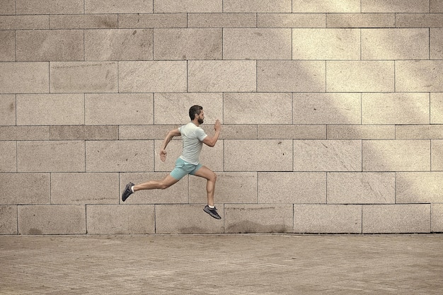 Uomo che corre all'aperto Corridore maschio sano sbrigati Ritratto a figura intera di ragazzo fitness che corre Raggiungimento del successo e dell'eccellenza Atleta che corre contro il muro di cemento L'uomo sportivo inizia a correre