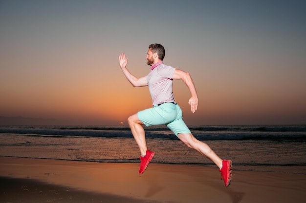 Uomo che corre sulla spiaggia al tramonto Giovane atletico che corre nella natura