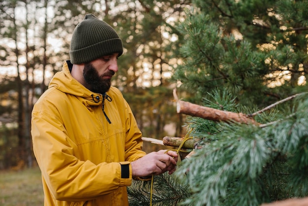 Uomo che costruisce un rifugio di sopravvivenza nella foresta Rifugio nei boschi dai rami di pino
