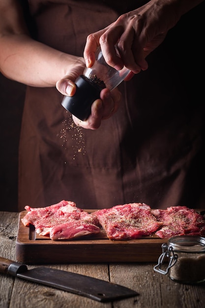 Uomo che cucina bistecche di carne in cucina. Lo chef sale e pepe su fondo di legno